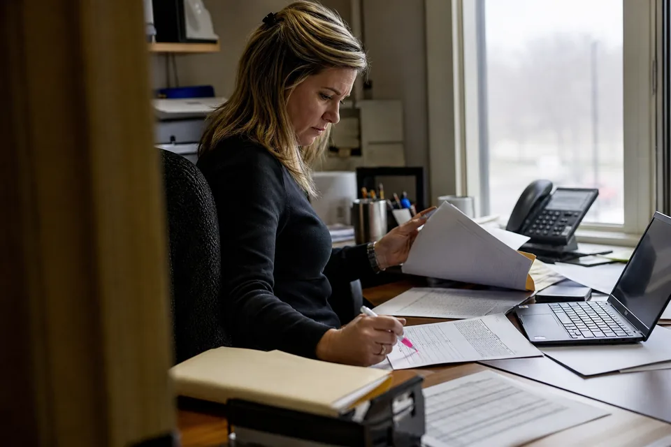 Accounts receivable manager reviewing an aged receivables printout and past-due invoices at her desk
